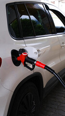 Fototapeta premium white car sports coupe is refueled to a gas station, a refueling gun in the filler neck of a gasoline tank car