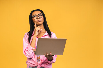 Young african american black thinking serious lady using laptop and smiling isolated over yellow background.