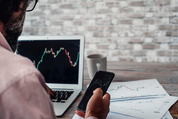 Stock and forex market business exchange with crypto currency business lifestyle. Back view of a man buying and selling stocks using laptop and mobile phone app technology connection. Economy job
