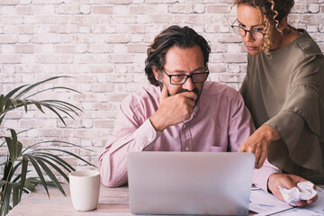 Two person couple looking at laptop display in work activity together. One man and a woman work with internet connection on a computer at the desk office workplace. Modern people team job worker