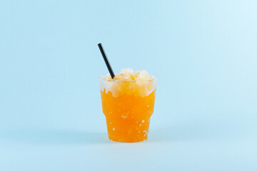 Refreshing Slushie drink. Orange Granizado in disposable plastic take away cup on blue background. Sweet citrus Shaved ice. Selective focus, copy space