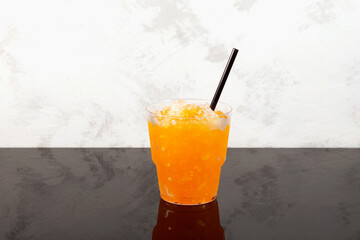 Sweet citrus Shaved ice. Orange Granizado in disposable plastic take away cup. Refreshing Slushie...