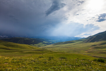 Endless pastures in the valley of the Assy plateau under thunderclouds with the sun