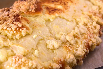 Close up of a large browned curd strudel (yeast-cake) with crumble. Cake freshly removed from the oven on a baking tray lined with paper. Shallow depth of field.