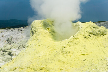 cone of sulfur deposits around a fumarole in a solfataric field illuminated by the sun against a...