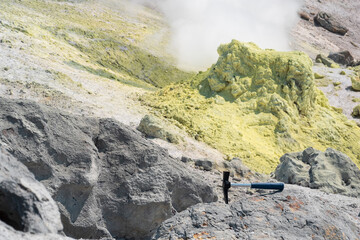 geological hammer in the rock against the backdrop of an steaming fumarole on the slope of a volcano