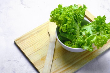 Lettuce placed in a white bowl and a cutting board on a white table. Vegetable salad. Vegetarian food. Clean food. Green vegetables.