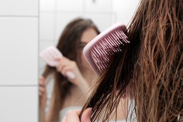 young beautiful girl in the bathroom with wet hair with a comb. in a white bath. hair care and health