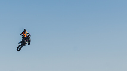 Fototapeta na wymiar Extreme sports concept. Bike rider jumping high in the air. Wide panoramic shot. Blue sky as a background. High quality photo