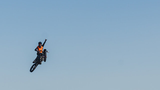 Adrenaline boost in extreme sports. Brave biker jumping extremely high on his black motorbike and waving with one hand. Blue sky as a background. High quality photo