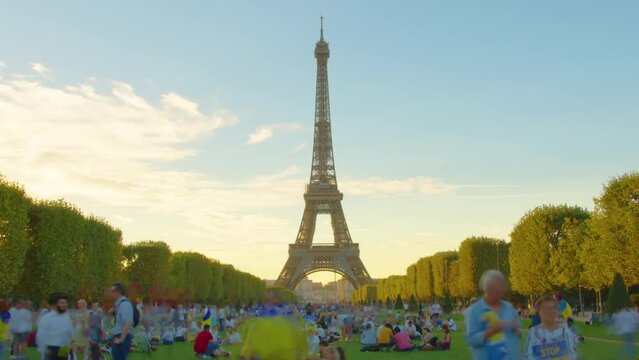 A timelapse of the Eiffel Tower along the river Seine. Eiffel Tower on Champs de Mars in Paris timelapse hyperlapse, France. Blue cloudy sky at summer day with green lawn and people walking around