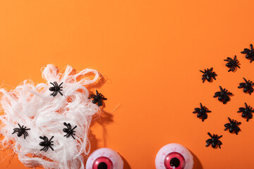 Multiple spider toys forming a spider web and scary eyes toys with copy space on orange background - Powered by Adobe