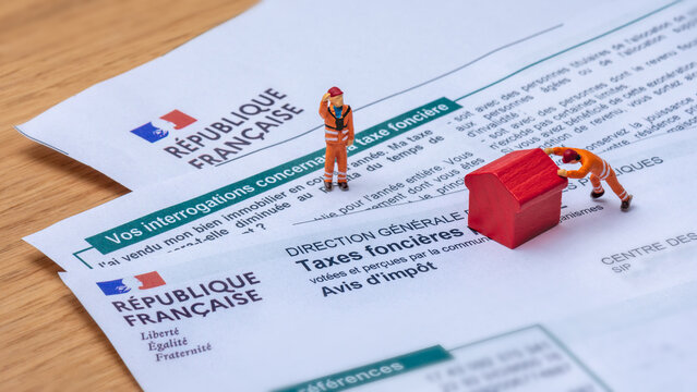 Clamart, France - 6 septembre 2022 : D&eacute;tail d'un avis d'imp&ocirc;t fran&ccedil;ais sur les taxes fonci&egrave;res avec de petits personnages d&eacute;pla&ccedil;ant une maison jouet rouge en bois
