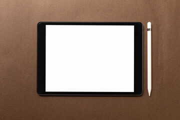 Black tablet with white blank screen is on top of brown paper with supplies. Top view, flat lay.