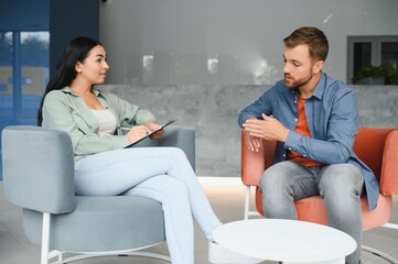 Psychologist talking with patient on therapy session. Depressed man speaking to a therapist while she is taking notes.