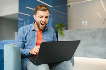 Photo of young excited man happy positive smile celebrate win victory success fists hands sit sofa home remote work.