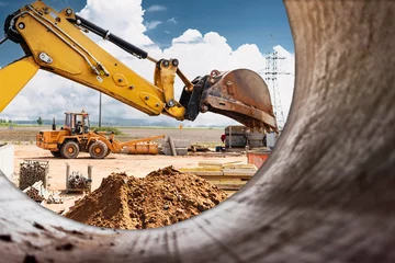 Fotobehang Vrachtwagen Excavator digs piles. Earthworks for the construction of the foundation. Construction equipment for the device of piles. Preparatory work for grillage. View from a large concrete pipe.  © Anoo