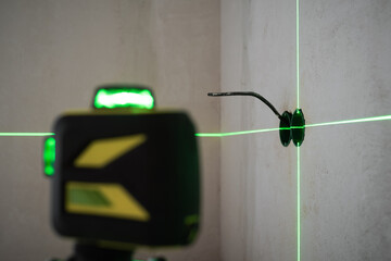 Electrical wiring work on the wall using laser level device. Plastic back boxes for sockets and switches leveled accurately to the green beam of laser level device. House construction and renovation
