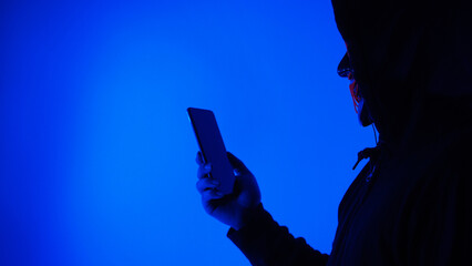 Digital security Concept. Anonymous hacker with mask holding smartphone hacked. Personal and Cyber...