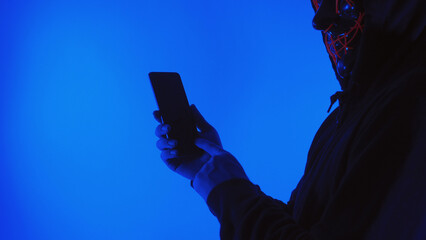 Digital security Concept. Anonymous hacker with mask holding smartphone hacked. Personal and Cyber...