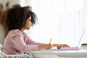 Smiling african american girl typing on laptop keyboard, side view