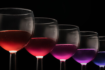 Multicolored glasses with different wines coctail - purple blue red on a black background glasses in a row