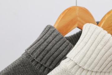 Sweaters hang on hangers on light background, close up
