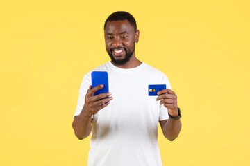 African Guy Shopping On Smartphone Holding Credit Card, Yellow Background