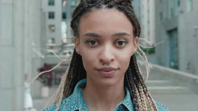 Close up portrait of young beautiful African American woman in a denim jacket with dreadlocks standing looking at camera smiling over business center background