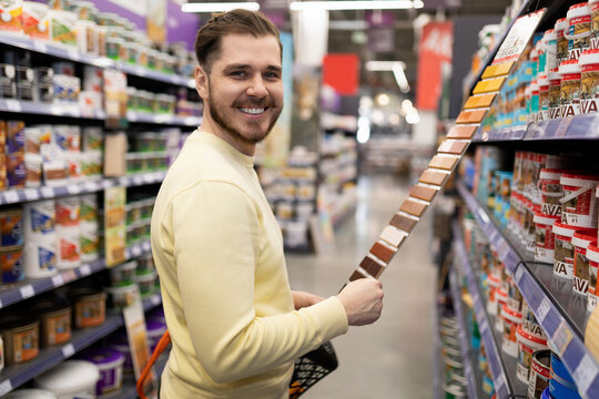 satisfied customer looking at camera at hardware store next to rows of renovation paint