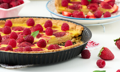 Round quiche with red strawberries and raspberries on a white table, top view