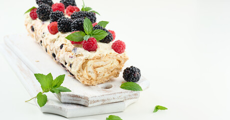 Baked meringue roll with cream and fresh fruits on a white wooden board, delicious dessert
