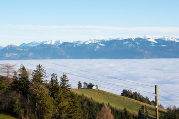 Beautiful landscape of swiss mountains and small cottage on a green hill, calm sea of fog