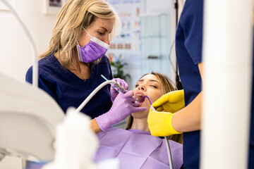 Female dentist with assistant working in dental clinic examining patient teeth.