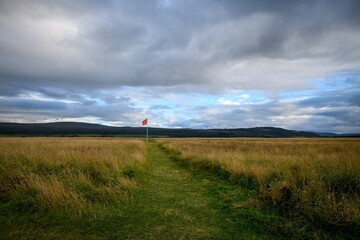 Culloden battlefield with a path leading to a red flag. Cloudy sky background.