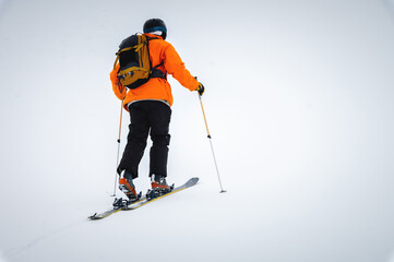 A skier climbs a snow-covered ridge in the fog with a backpack, ski tour. Extreme sport in the...
