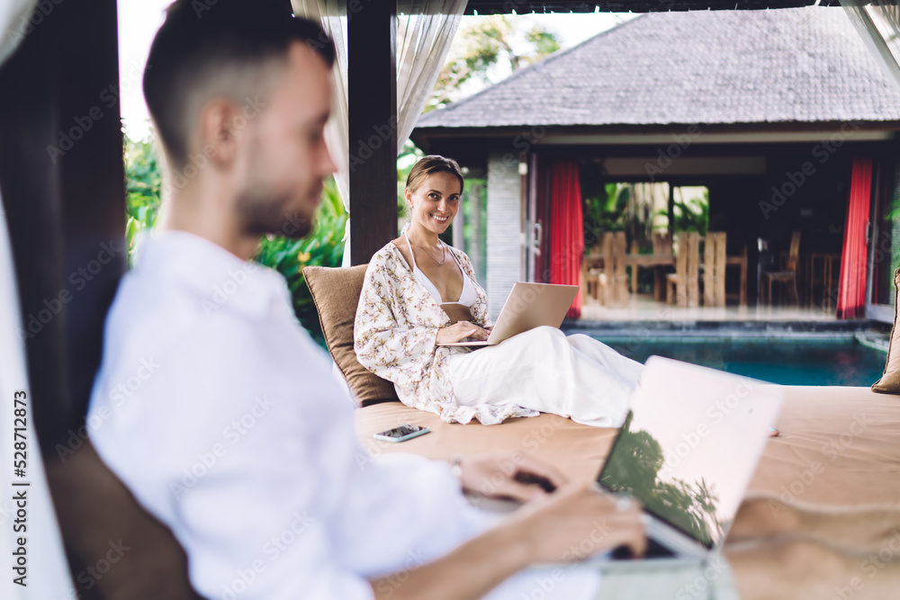 Poster portrait of cheerful caucaisan woman smiling at camera while working remotely together with blurred 