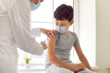 Child getting antiviral vaccine. Nurse or doctor giving shot to little kid. School boy in facemask...