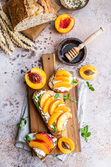 Open sandwiches with tartine bread and cream cheese, nectarine and apricot drizzled with honey on wooden cutting board. Top view.