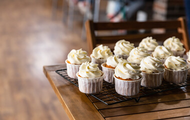 Beautiful vanilla cupcakes with cream cheese frosting on metal grille. Delicious homemade dessert. Festive bakery. Blurred background.