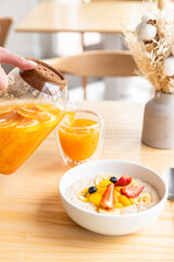 Healthy breakfast in cafe with oatmeal porridge with berries, banana and mango in bowl and spicy sea buckthorn tea. Modern minimal scandinavian interior.
