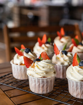 Cupcakes with white icing decorated with strawberries, blueberries and mint. Delicious homemade dessert. Festive bakery. Blurred background.
