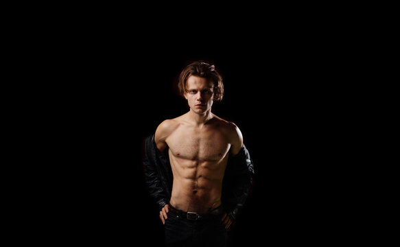 muscular athletic man with a naked torso and inflated abdominal muscles on a black background. Sexy man with long hair.