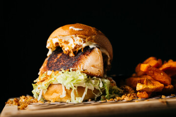 Bacon burger with lettuce accompanied with sweet potatoes on a wooden table and over a black background