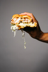 Human hand holding a bitten pork burger with lettuce over a grey background