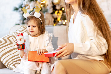 Mom and daughter toddler sitting on the couch near the decorated Christmas tree open gifts.Family. Christmas holidays