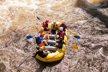 Top view of a rowers team with an oars overcomes rapids on a stormy river on an inflatable rafting boat - obrazy, fototapety, plakaty