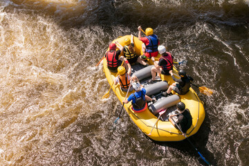 Top view of a rowers team with an oars overcomes rapids on a stormy river on an inflatable rafting boat - obrazy, fototapety, plakaty