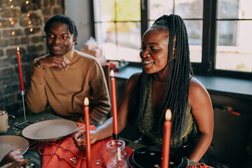 Best friends celebrating new year. Young people with candles, sitting at dining table. Diverse students during christmas party at home, smiling and laughing.