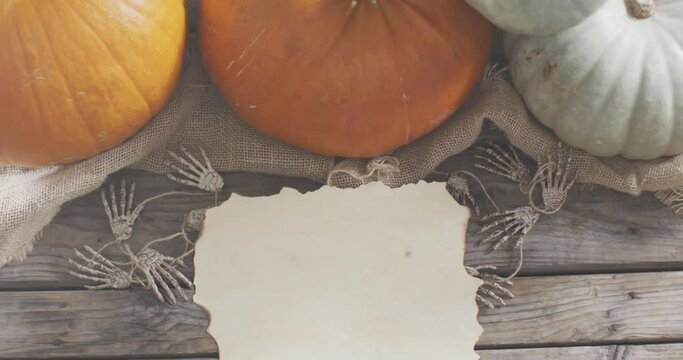 Paper with copy space against skeleton hands and pumpkins on wooden surface